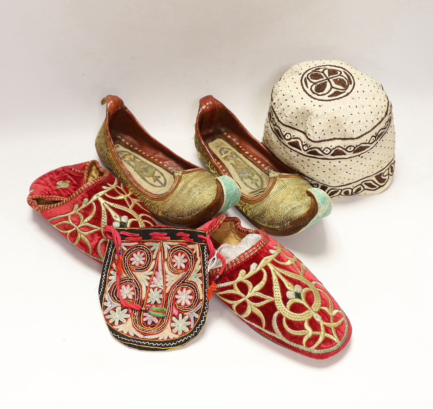 A pair of early 20th century metal thread embroidered Turkish slippers, a pair of similar embroidered red velvet children’s Indian slippers, an embroidered chain stitch drawstring purse and a quilted child’s hat